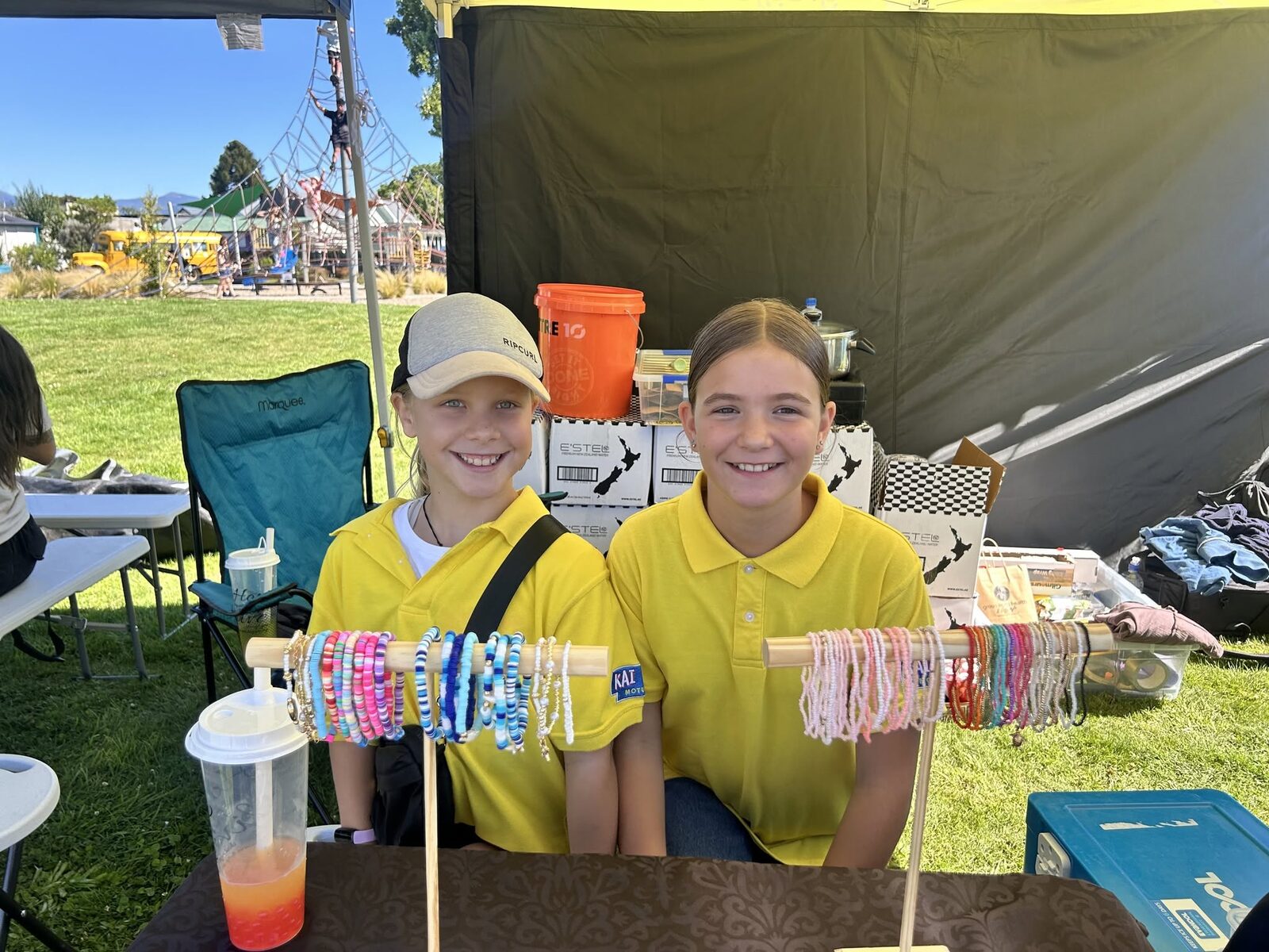 Two young stallholders smiling behind a rack of handmade beaded bracelets